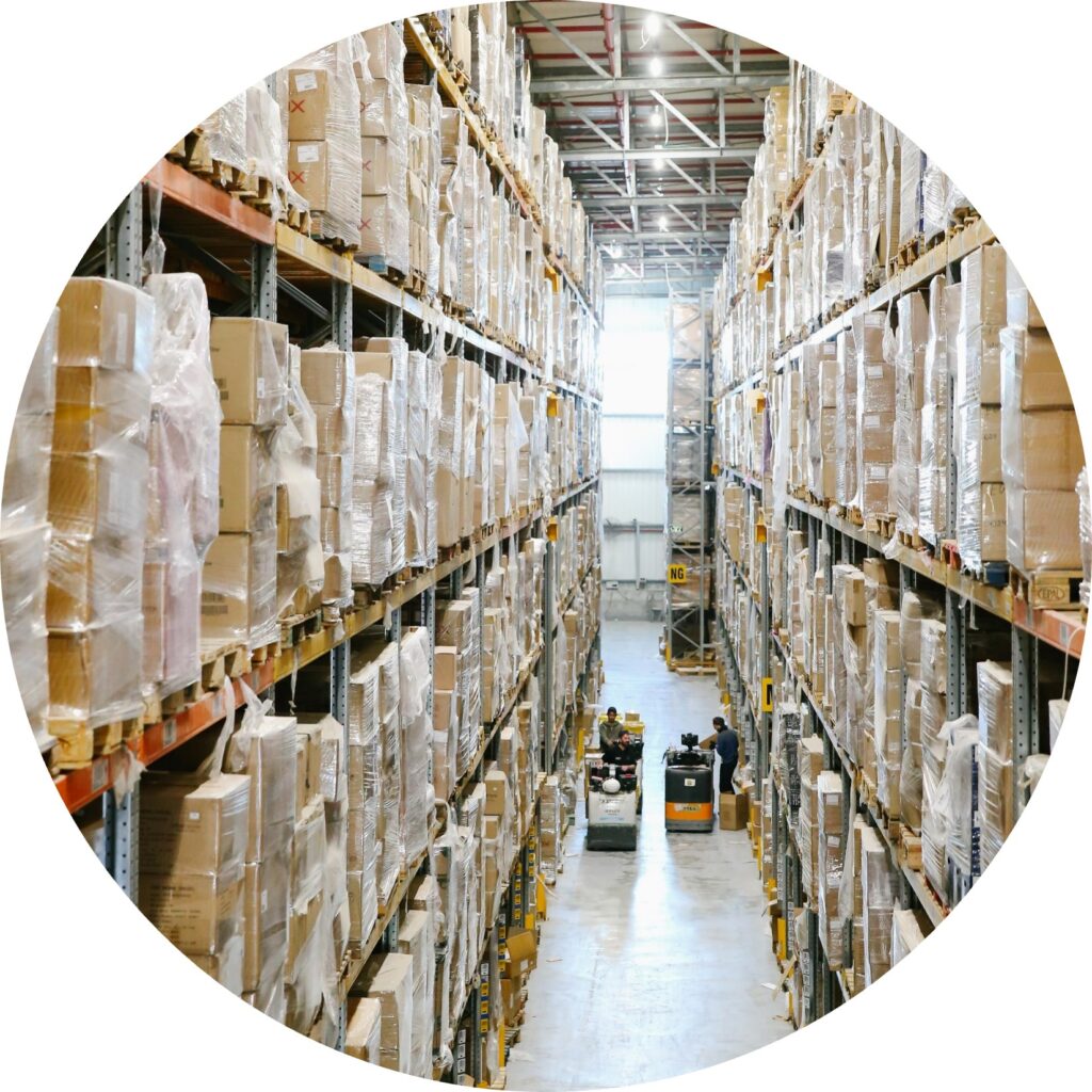 A look down an aisle of a warehouse. Two forklift drivers are driving past one another.