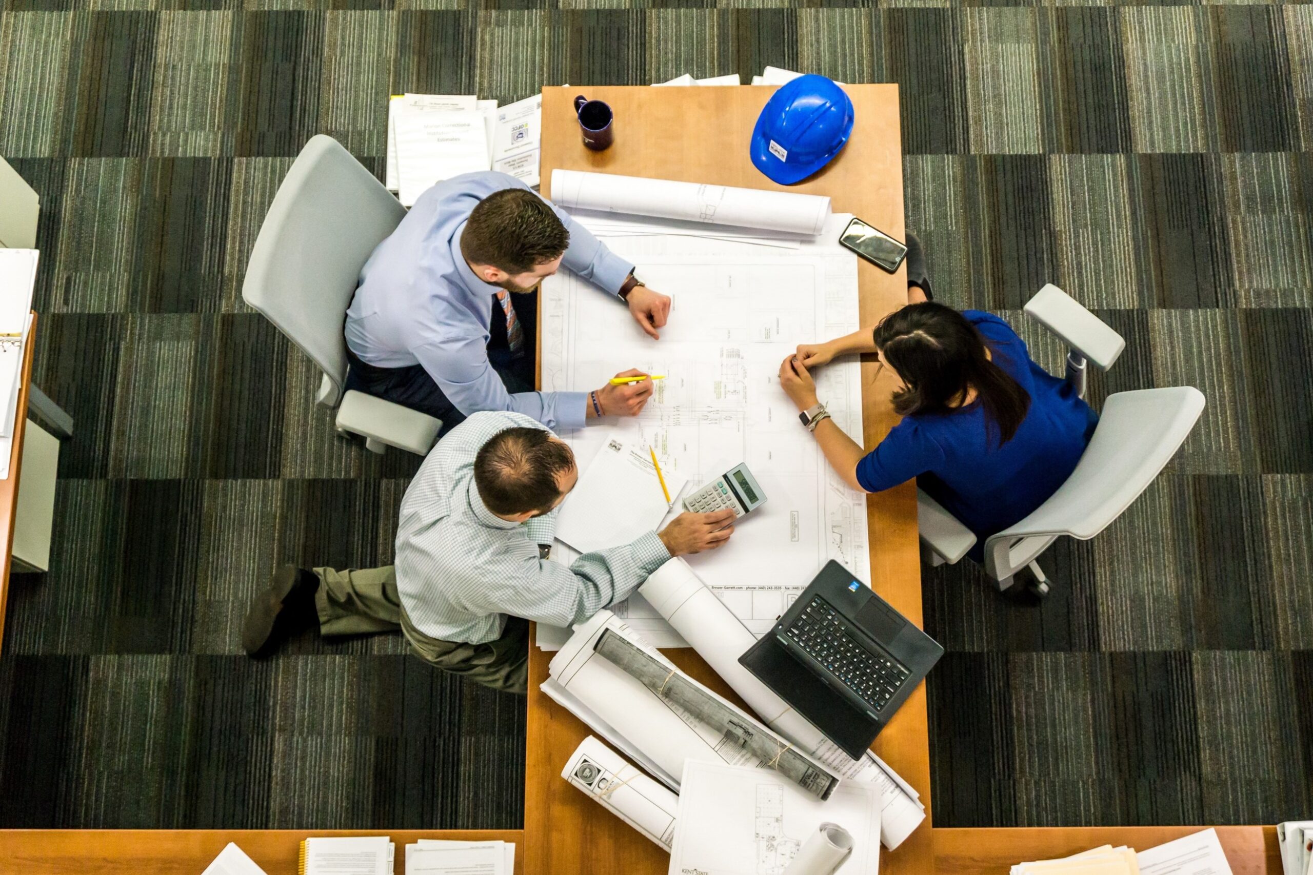 An overhead shot of three people looking over a large document.